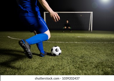 Legs of a soccer player about to kick off the soccer ball from the green grassy sports field towards the goalpost