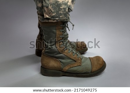 Legs of a soldier in camouflage and army boots on a gray background. Military conflicts and crises. Close-up. 