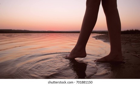 Legs splash in water against red evening sunset. Slow motion