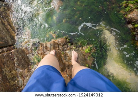 Legs stand on rock  covered with sea grass and waves