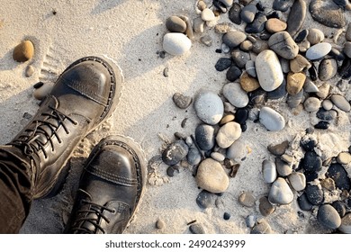 Legs of a standing female in rocker boots on beach sand with various rocks and pebbles top down view in sunset light - Powered by Shutterstock