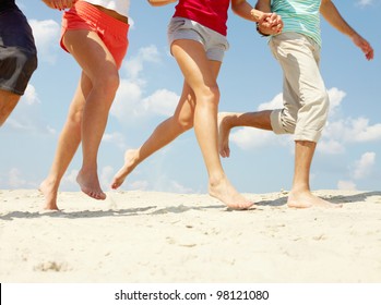 Legs Of Three Friends Running On Beach In Summer