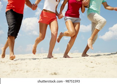 Legs Of Three Friends Running On Beach In Summer