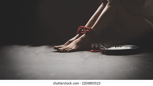 Legs Of A Tortured, Rope Bound Asian Woman Sit Unhappy And Despairing In Freedom With Plates Food On The Side To Survive : Asian Women Trafficking And Illegal Immigration.