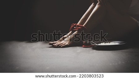 Legs of a tortured, rope bound asian woman sit unhappy and despairing in freedom with plates food on the side to survive : Asian women trafficking and illegal immigration.