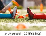 Legs of two soccer players in red and blue soccer socks and cleats sitting on the training ground. Kids on football soccer training pitch. School boys practicing sports on physical education class
