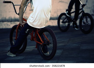 Legs of two teenager boys sitting on orange and black bmx low bicycles on street summer male sports activity outdoor closeup on natural background, horizontal picture 
