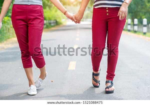 \
The\
legs of two women holding hands walking on the\
road