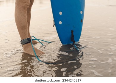 Legs of unrecognizable man standing on sandy seaside with blue leash attached to ankle and holding mazarine surfboard. Surfboarder with rope on leg preparing for surfing on beach near sea. - Powered by Shutterstock