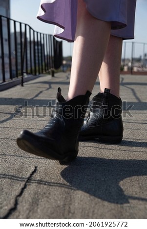 Legs of white woman in skirt and black boots on the pavement