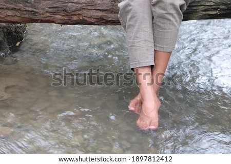 Legs of a woman in pants who sitting on a wood bridge and swinging her feet in a river