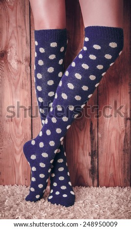 Legs of a woman in a purple polka dot golfs on the carpet on the wooden background. Vintage toning