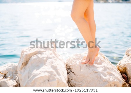 Legs of a woman standing on a stone near the water on a rocky beach 
