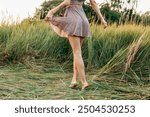 Legs of a woman walking barefoot on the grass in a summer dress in a field with grass