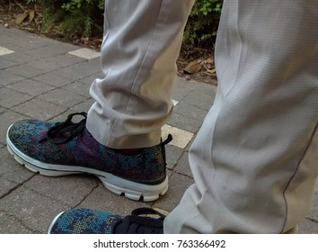 Legs of woman walking on brick sidewalk, in beige pants and shoes with colorful dots in purple, blue, green and yellow with black shoelaces   - Powered by Shutterstock