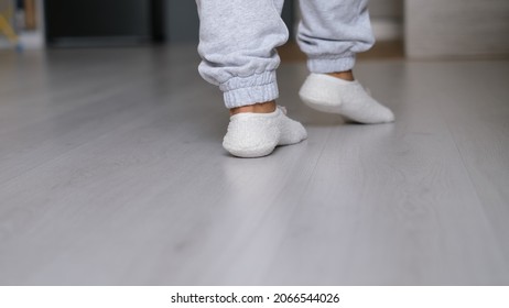 Legs Of A Woman In White Socks Walking On The Wooden Floor Of Her House With A Sofa In The Background. Feet Wearing White Socks On Gray Wooden Floor