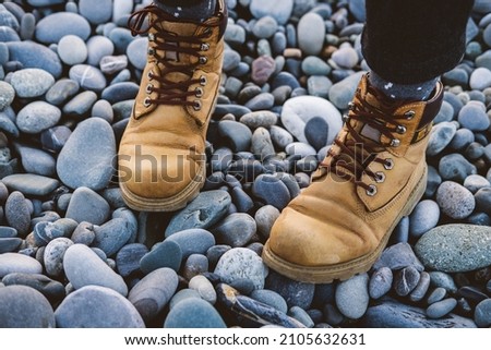 Legs in yellow rough hiking boots on the pebble beach. Travel concept.