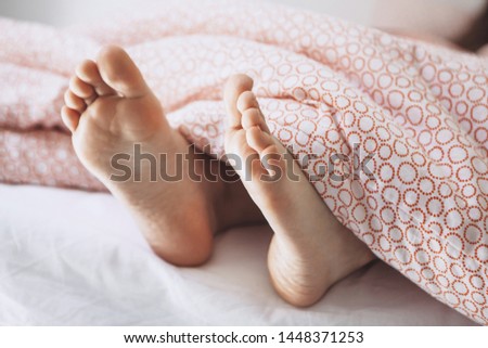 Legs of young adult girl under the blanket close up. She is sleeping.
