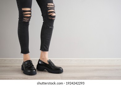 Legs of a young girl in black jeans and black shoes on a gray background, space for text.