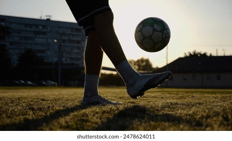 Legs of young man kicking ball at green field. Male feet of professional footballer juggling soccer ball on stadium at sunset. Sportsman practicing tricks outdoor. Concept of a freestyle football - Powered by Shutterstock