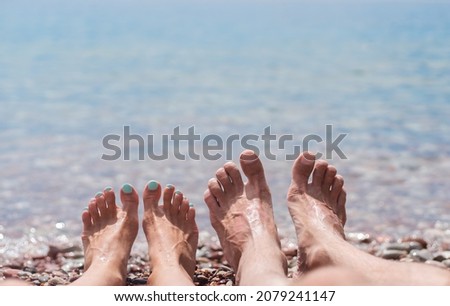 Legs of young man and woman on the beach by the sea. Enjoying the sun on a summer sunny day at the sea. Family vacation concept and travel. Close-up. Copy space.