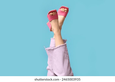 Legs of young woman in jeans and pink open-toed high heels on blue background