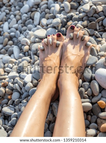 Legs of young woman resting on the sea beach. Small pebbles are inserted between your fingers for fun