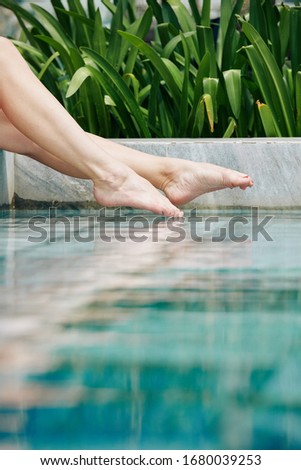 Legs of young woman splashing water in swimming pool