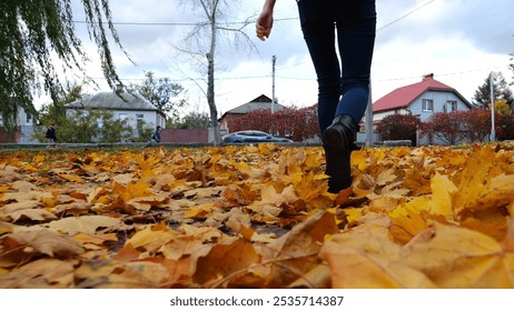 Legs of young woman stepping on yellow foliage at park. Female feet in boots going on fallen maple leaves at parkland. Girl walking at parkland at autumn season on cloudy day. Close up Slow motion - Powered by Shutterstock