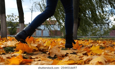 Legs of young woman stepping on yellow foliage at park. Female feet in boots going on fallen maple leaves at parkland. Girl walking at parkland at autumn season on cloudy day. Close up Slow motion - Powered by Shutterstock