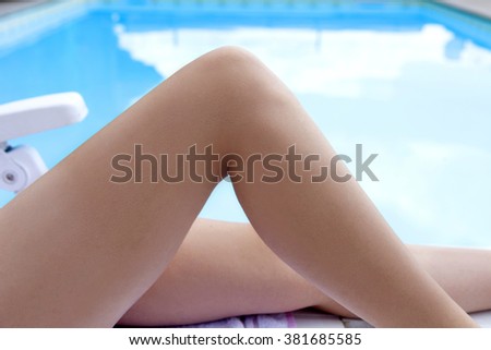 Legs of young woman sun tanning beside swimming pool 