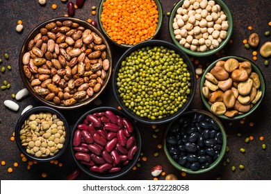 Legumes, lentils, chikpea and beans assortment in different bowls on stone table. Top view.