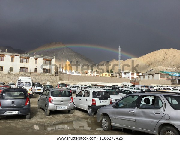 Leh Ladakh ,\
India-July26,2018:Tourist cars parked at the parking lot. In the\
town of Leh Ladakh, the day is raining and there is a rainbow\
across the city.