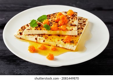 Leipajuusto, kaffeost, bread cheese, finnish squeaky cheese slices with cloudberry jam and fresh mint on a white plate on a black wooden table