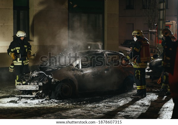 LEIPZIG, GERMANY - 12.04.2020: Firefighters inspect\
a burn out car at\
night