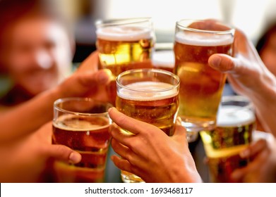 leisure, drinks, celebration, people and holidays concept - smiling friends drinking beer and stitching glasses in a restaurant or pub
