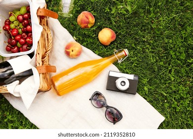 leisure, food and drinks concept - close up of picnic basket, bottle of fruit juice with sunglasses and film camera on grass