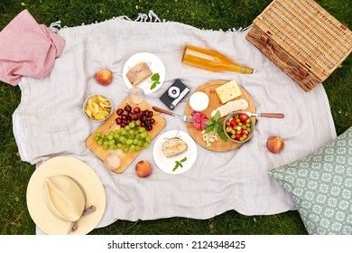 leisure, food and drinks concept - close up of snacks, camera and picnic basket on blanket on blanket