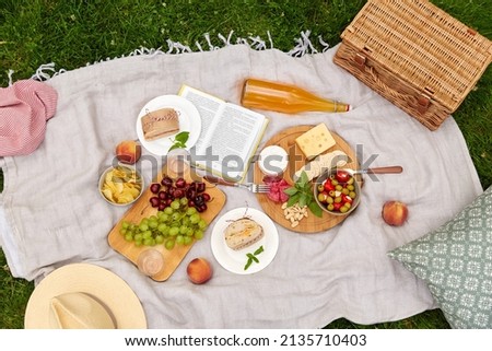 leisure, food and drinks concept - close up of snacks and picnic basket on blanket on grass at summer park