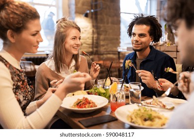 leisure, food, drinks, people and holidays concept - happy friends eating and drinking at restaurant