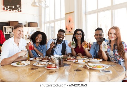 Leisure, Food And People Concept - Group Of Happy International Friends With Drinks Eating At Restaurant Table