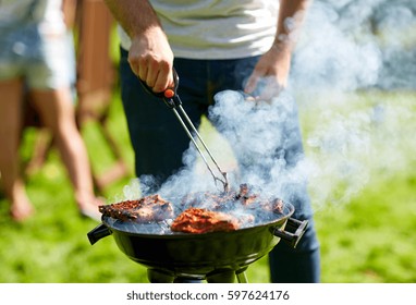 leisure, food, people and holidays concept - man cooking meat on barbecue grill at outdoor summer party