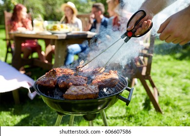 leisure, food, people and holidays concept - man cooking meat on barbecue grill for his friends at summer outdoor party - Powered by Shutterstock