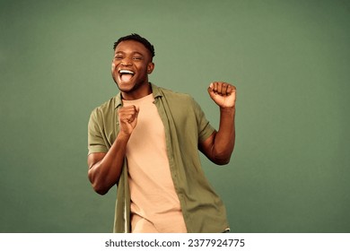 Leisure with fun. Energetic african american gun in casual wear actively dancing with flexible body over green studio background. Joyful young man having fun while perfectly feeling music beat.