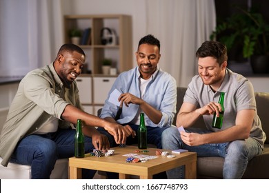 leisure games, friendship and gambling concept - happy male friends playing cards and drinking beer at home at night