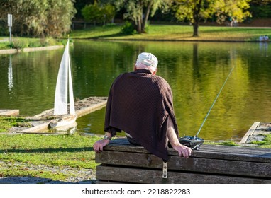 Leisure And Hobbies In Old Age: Seniors, Pensioners Sitting By The Lake With A Model Boat, Sailing Boat And Remote Control