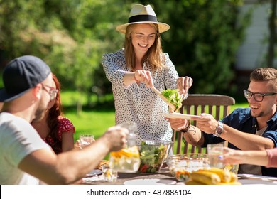 Leisure, Holidays, Eating, People And Food Concept - Happy Friends Having Dinner And Sharing Salad At Summer Garden Party