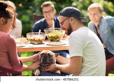 Leisure, Holidays, Eating, People And Food Concept - Happy Friends With French Bulldog Dog Having Dinner At Summer Garden Party