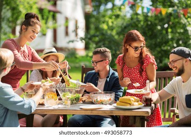 Leisure, Holidays, Eating, People And Food Concept - Happy Friends Having Dinner And Sharing Salad At Summer Garden Party