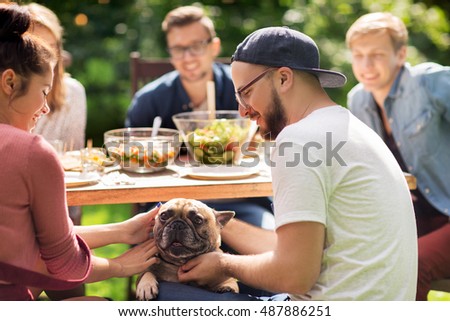 leisure, holidays, eating, people and food concept - happy friends with french bulldog dog having dinner at summer garden party